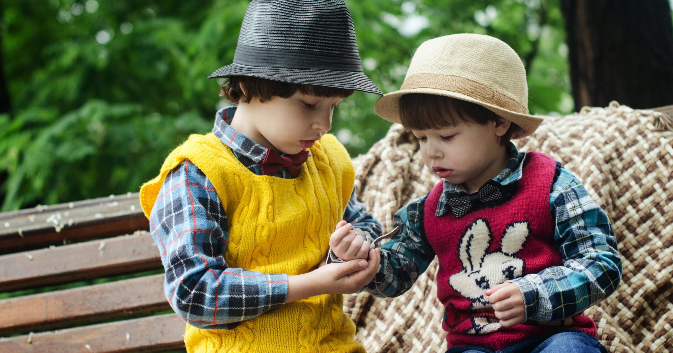 Two young boys in colorful sweaters and hats, sharing and playing outdoors.