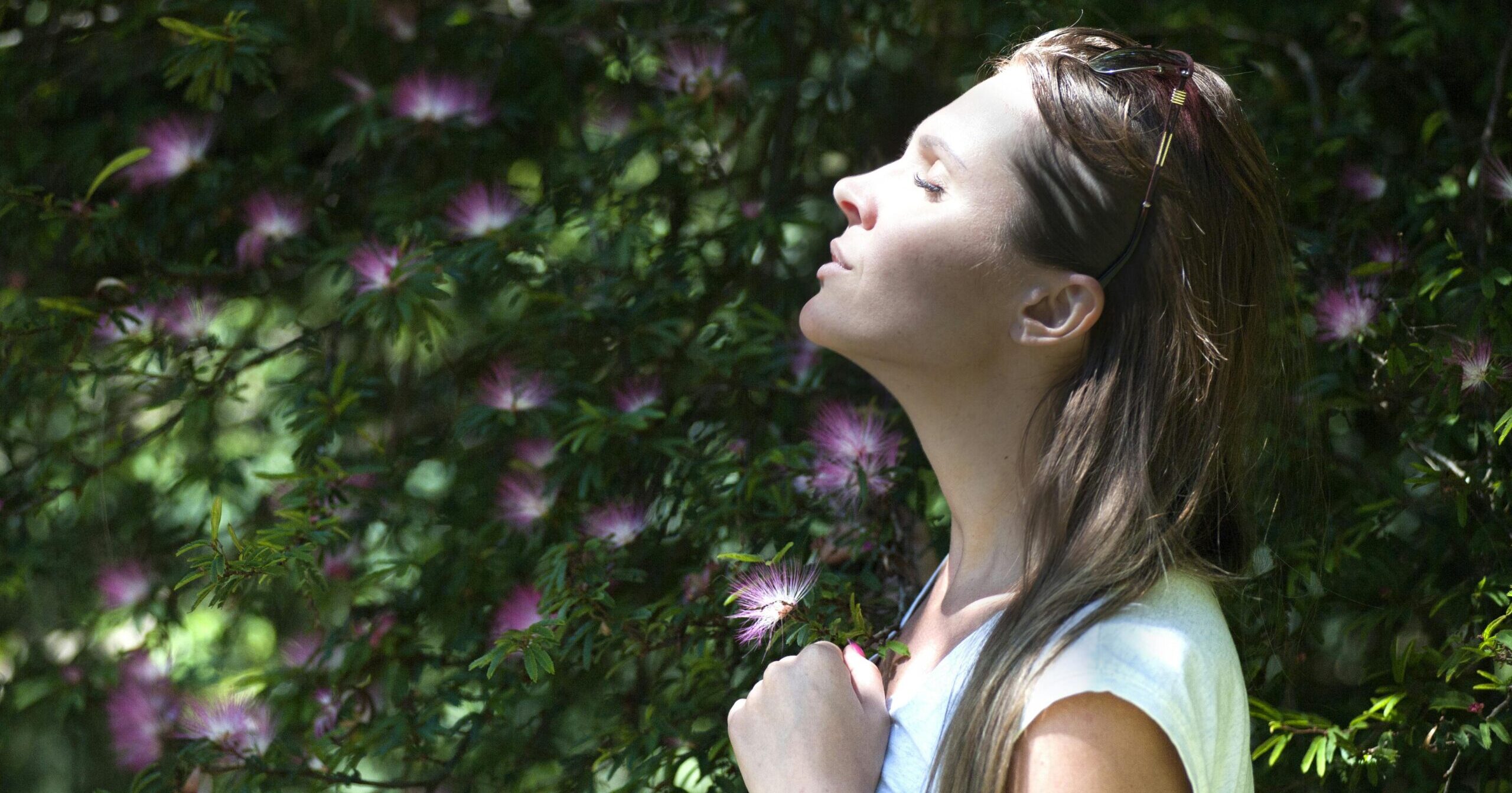 A woman enjoying a serene moment in a sunlit garden, surrounded by vibrant flowers.